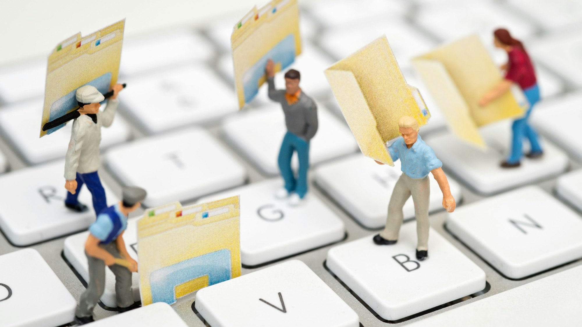 Kleine Männchen stehen mit ausgedruckten Datei-Symbolen auf einer Tastatur