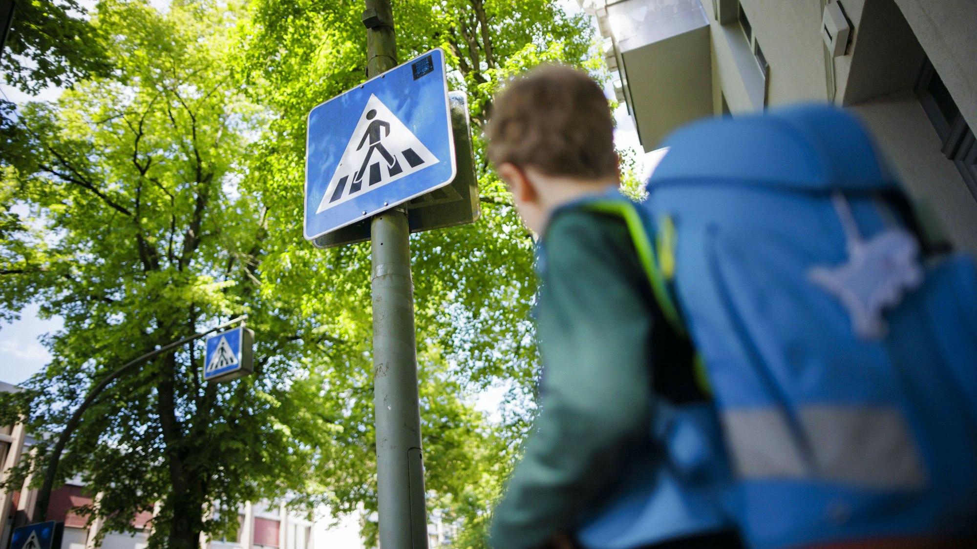 Ein Schulkind steht mit Schulranzen vor einem Zebrastrreifen-Schild.