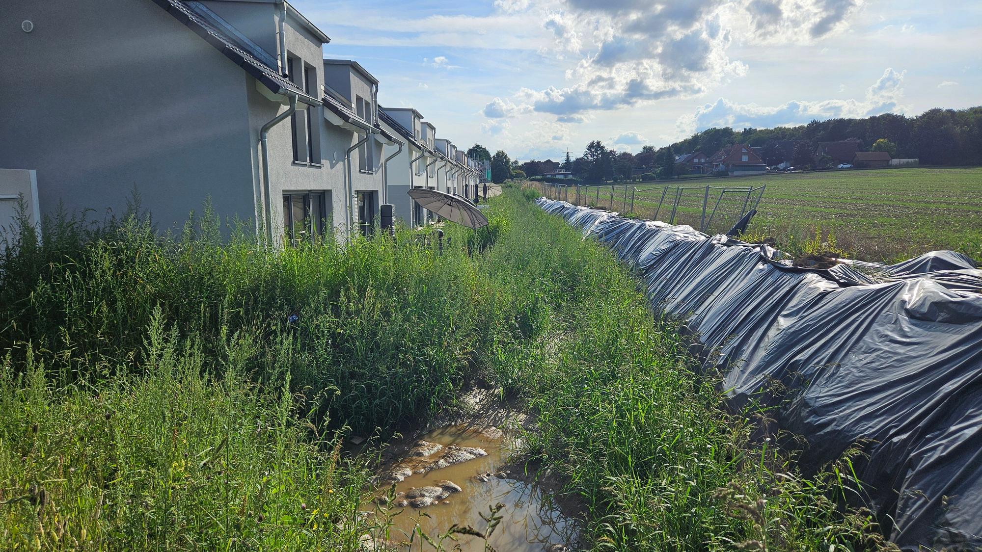 Ein provisorischer Erdwall hält das Wasser von einem Acker ab und schützt Häuser.