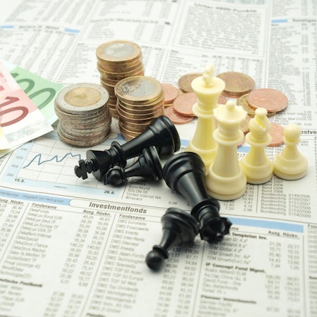 Geldscheine, Münzstapel und Schachfiguren liegen auf einer Zeitungsseite mit Börsenzahlen.