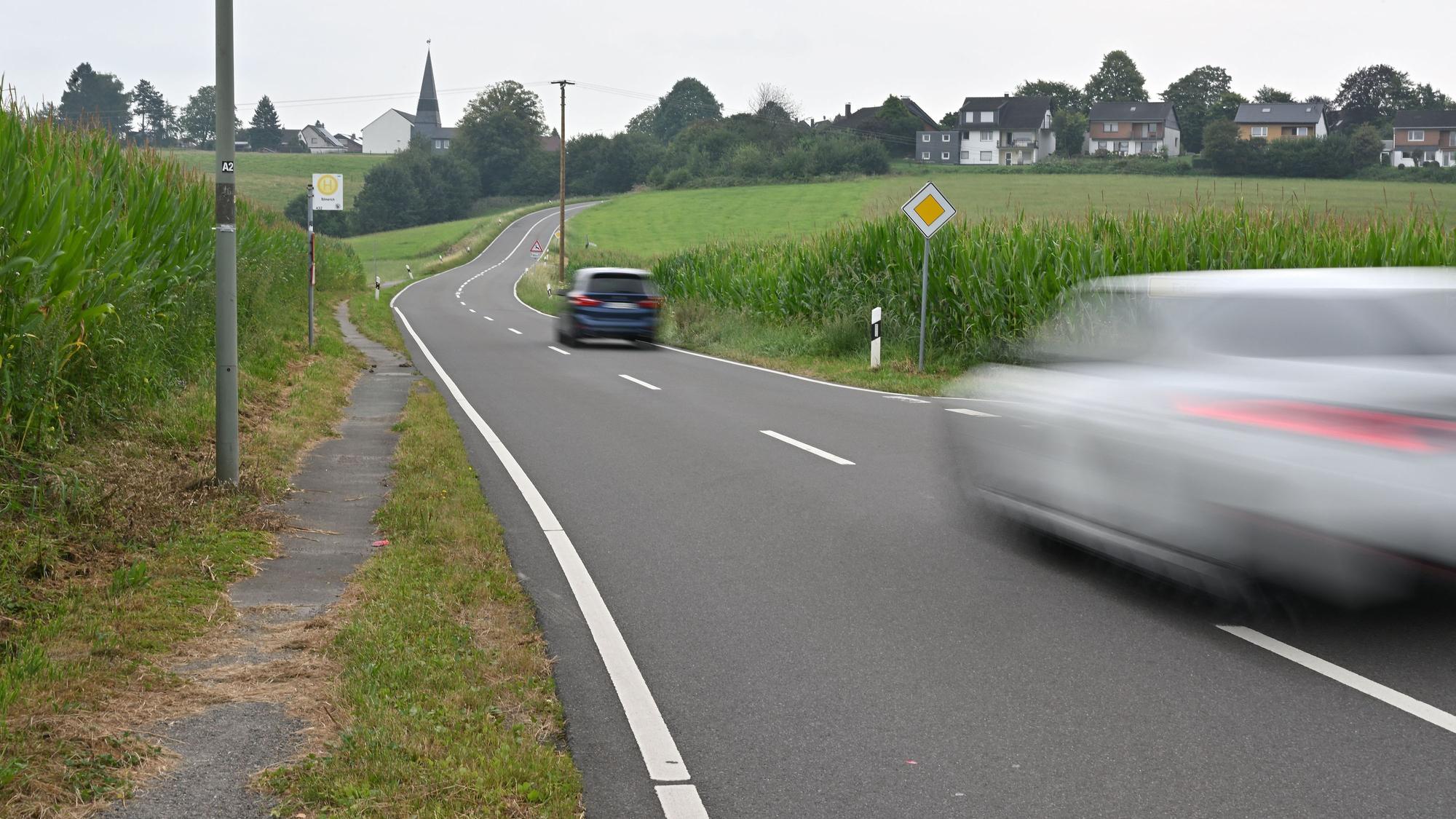 Eine Landstraße. Auf ihr zwei Autos, am Rand nur ein schmaler Trampelpfad für Fußgänger.