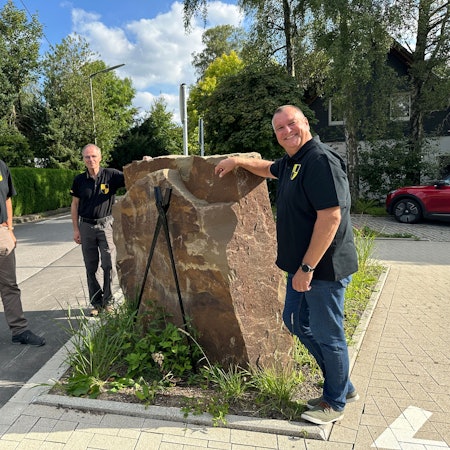 Jörg Jansen, Harald Langusch und Ulrich Gärtner stehen um eine Skulptur auf dem Dorfplatz.
