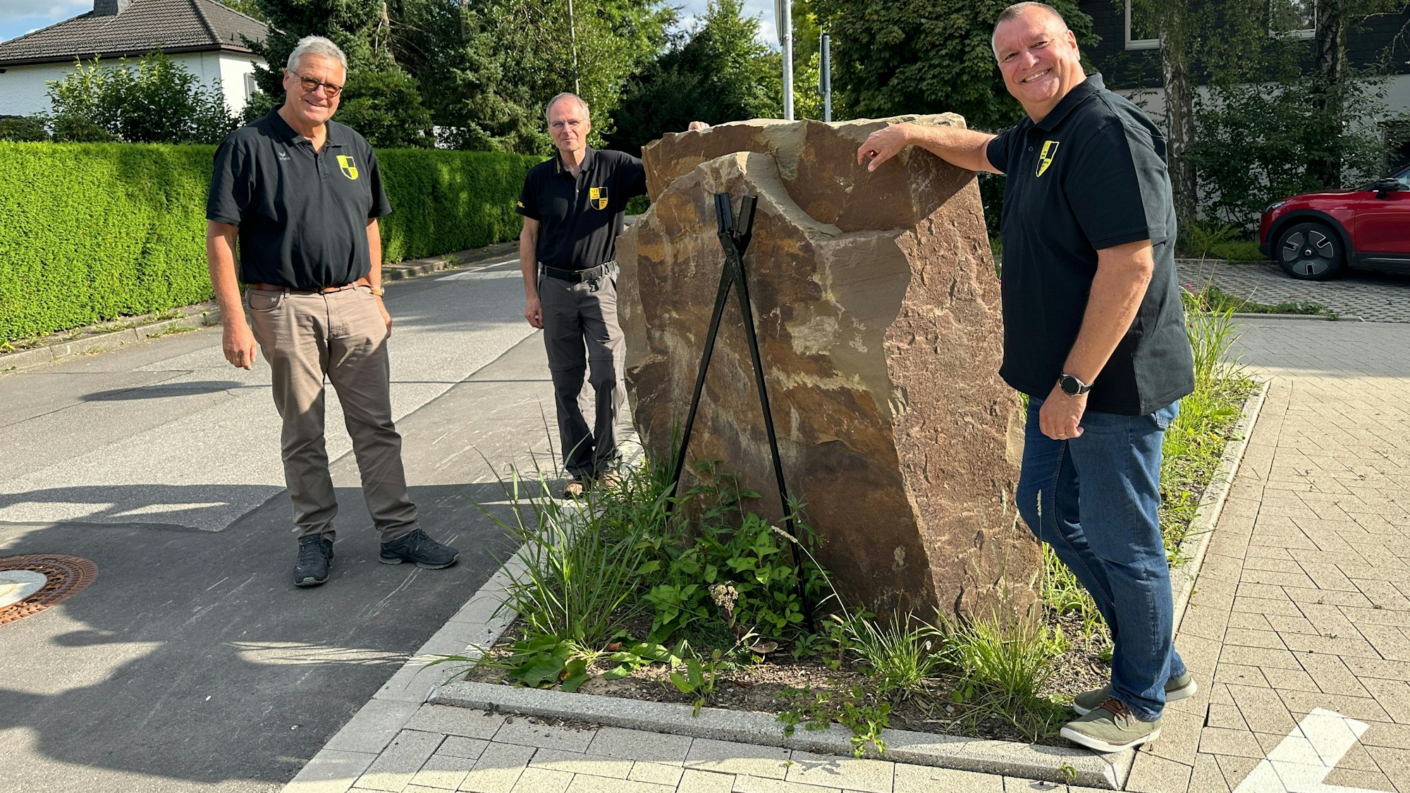 Jörg Jansen, Harald Langusch und  Ulrich Gärtner stehen um eine Skulptur auf dem Dorfplatz.