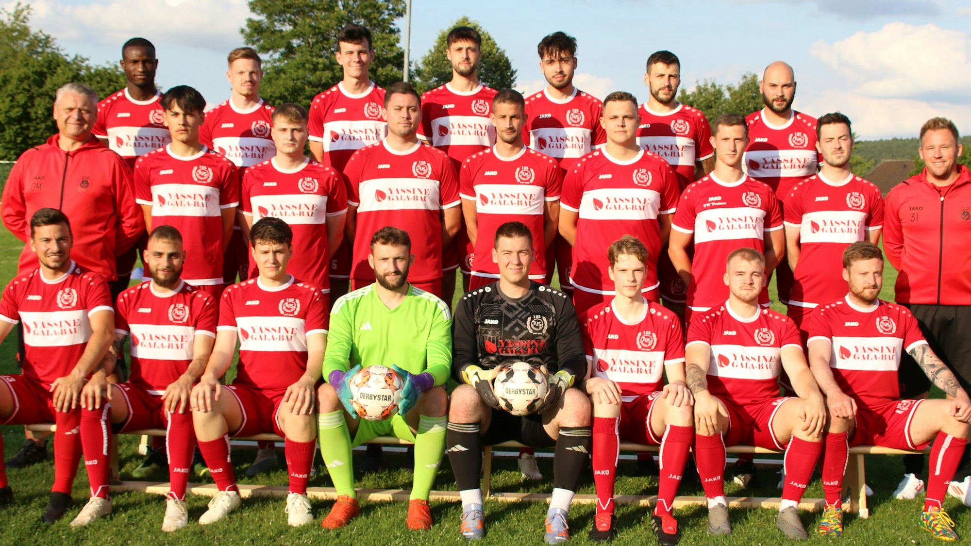 Die TuS Mechernich posiert auf einem Rasen und vor einem leicht bewölkten Himmel.