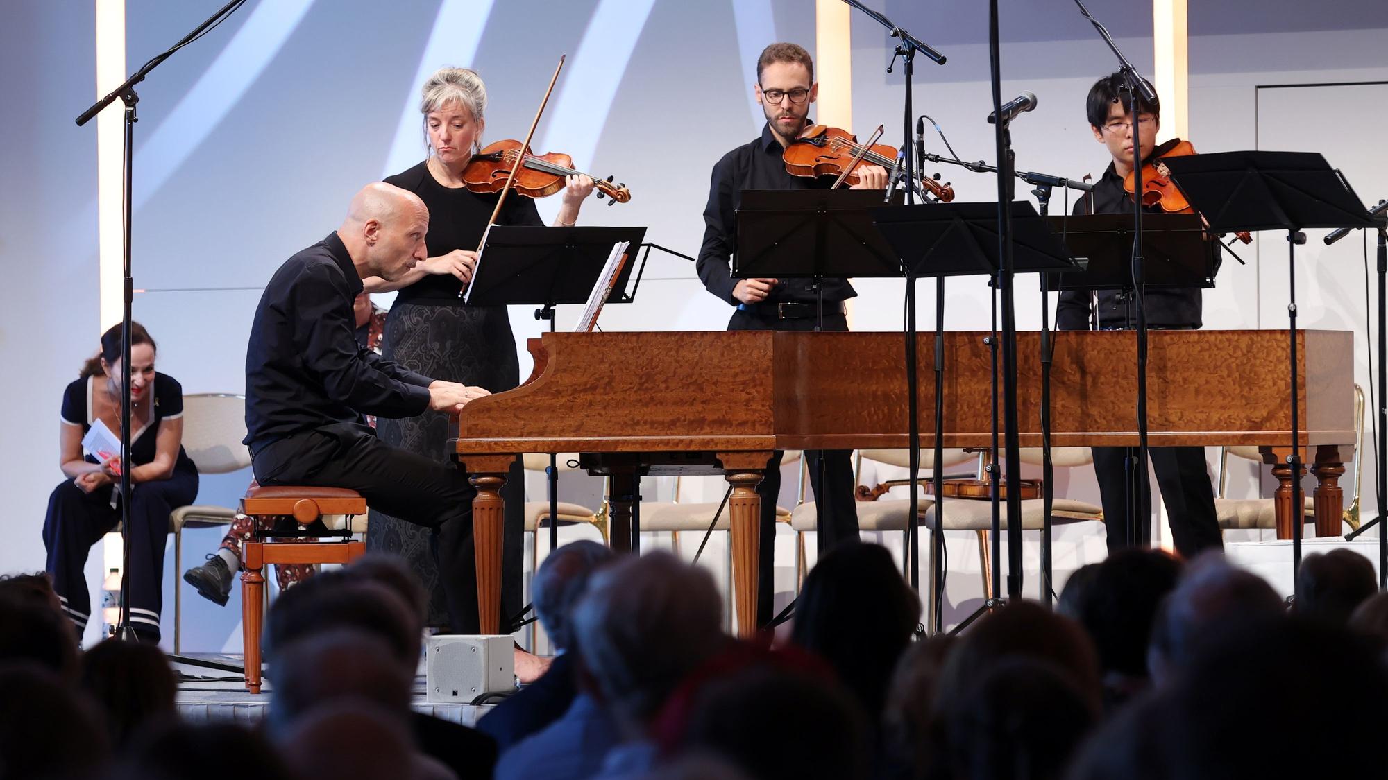 Musiker stehen auf einer Bühne, im Vordergrund spielt jemand Cembalo