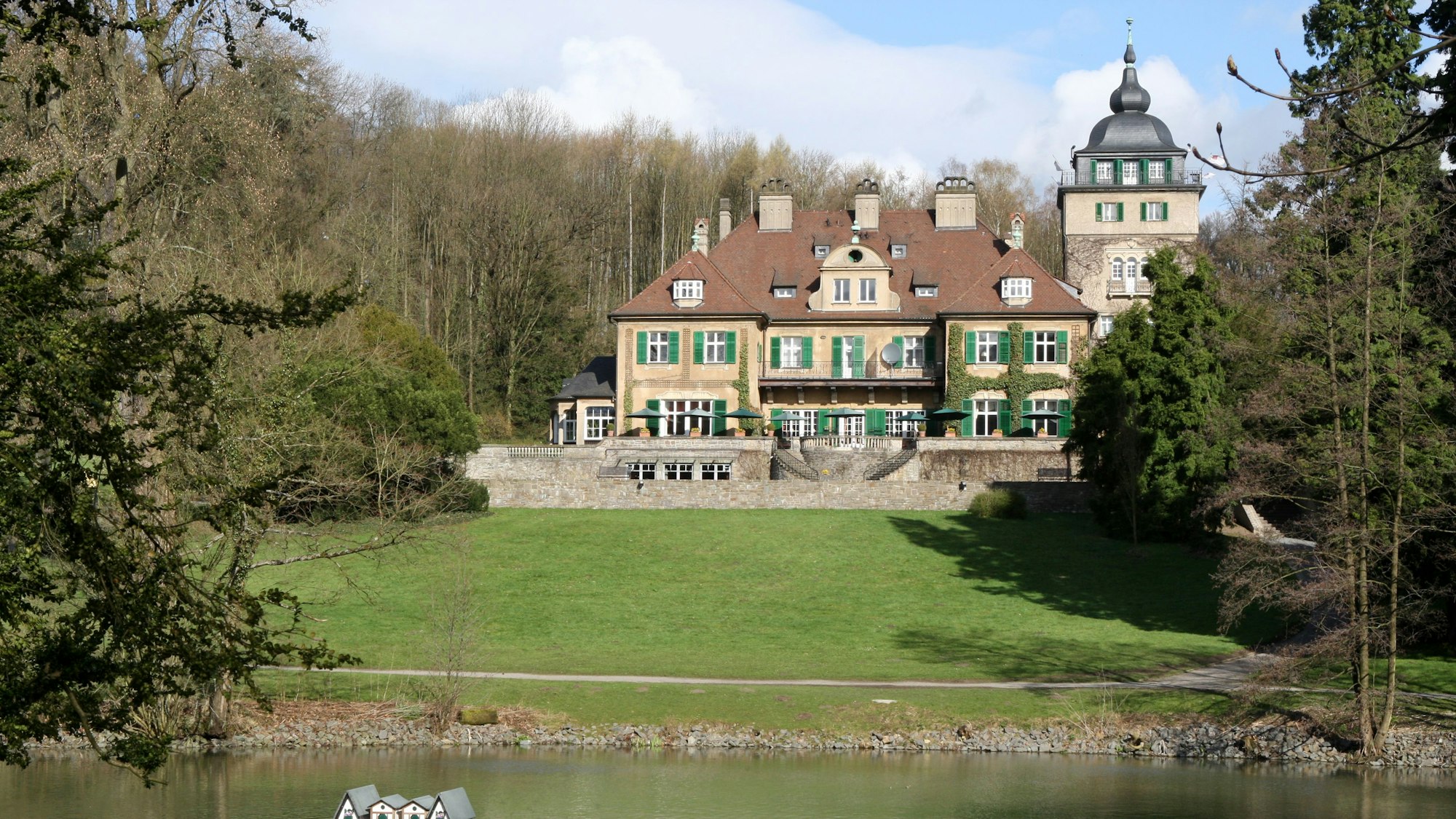 Hinter einem Teich und einer Wiese ist das Schlosshotel Lerbach in Bergisch Gladbach zu sehen.