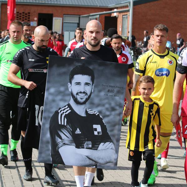 Die Spieler gehen von der Kabine auf den Platz. Einer trägt ein schwarz-weißes Foto des verunglückten Spielers.