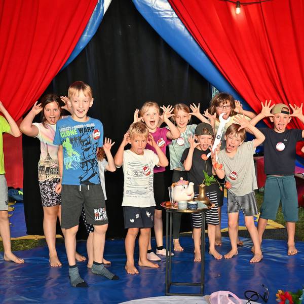 Ein Zirkuszelt. In der Manege eine Gruppe von Kindern, die Grimassen schneiden.