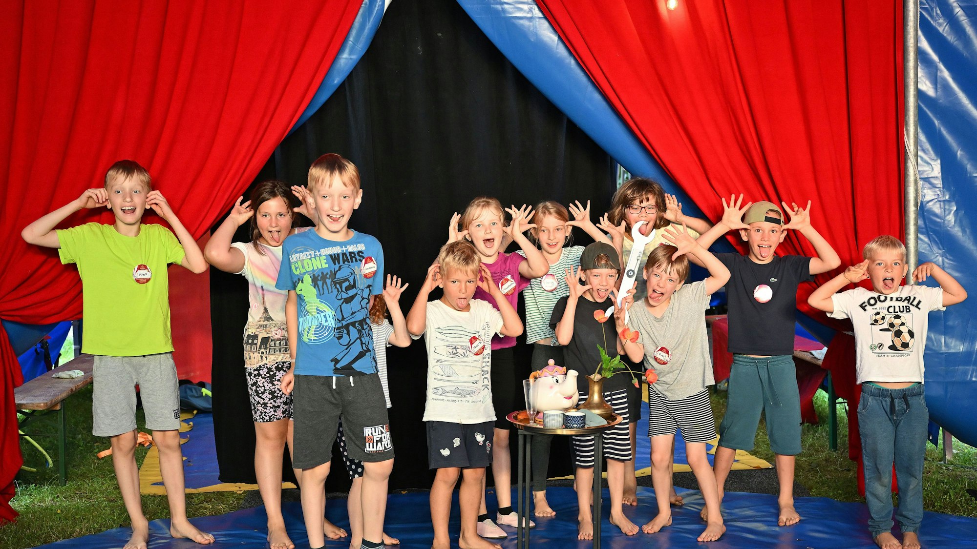 Ein Zirkuszelt. In der Manege eine Gruppe von Kindern, die Grimassen schneiden.