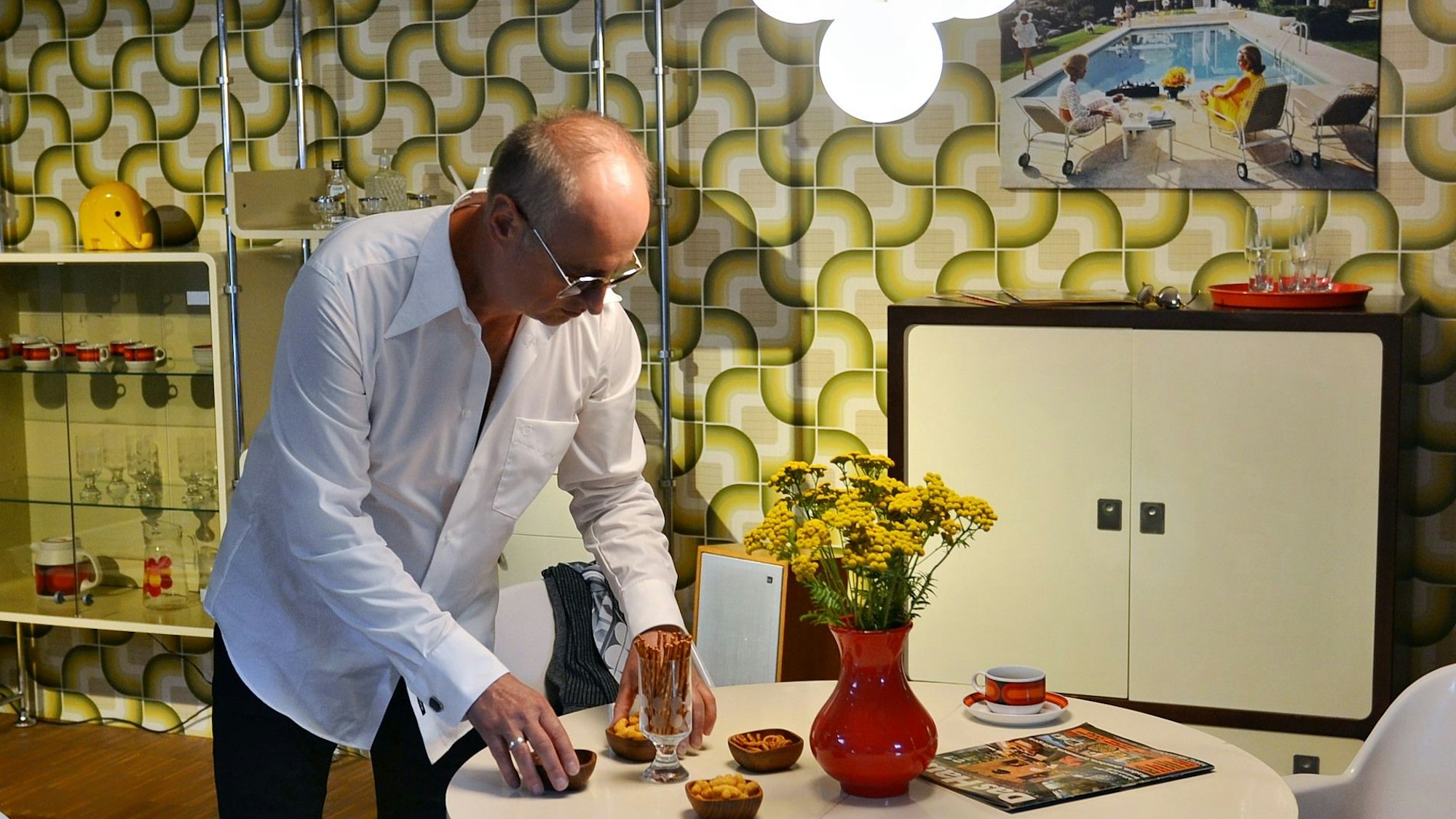 Ein Darsteller richtet im Rahmen der gespielten Geschichte im Wohnzimmer Snacks bei der Zeitblende 1974 an.