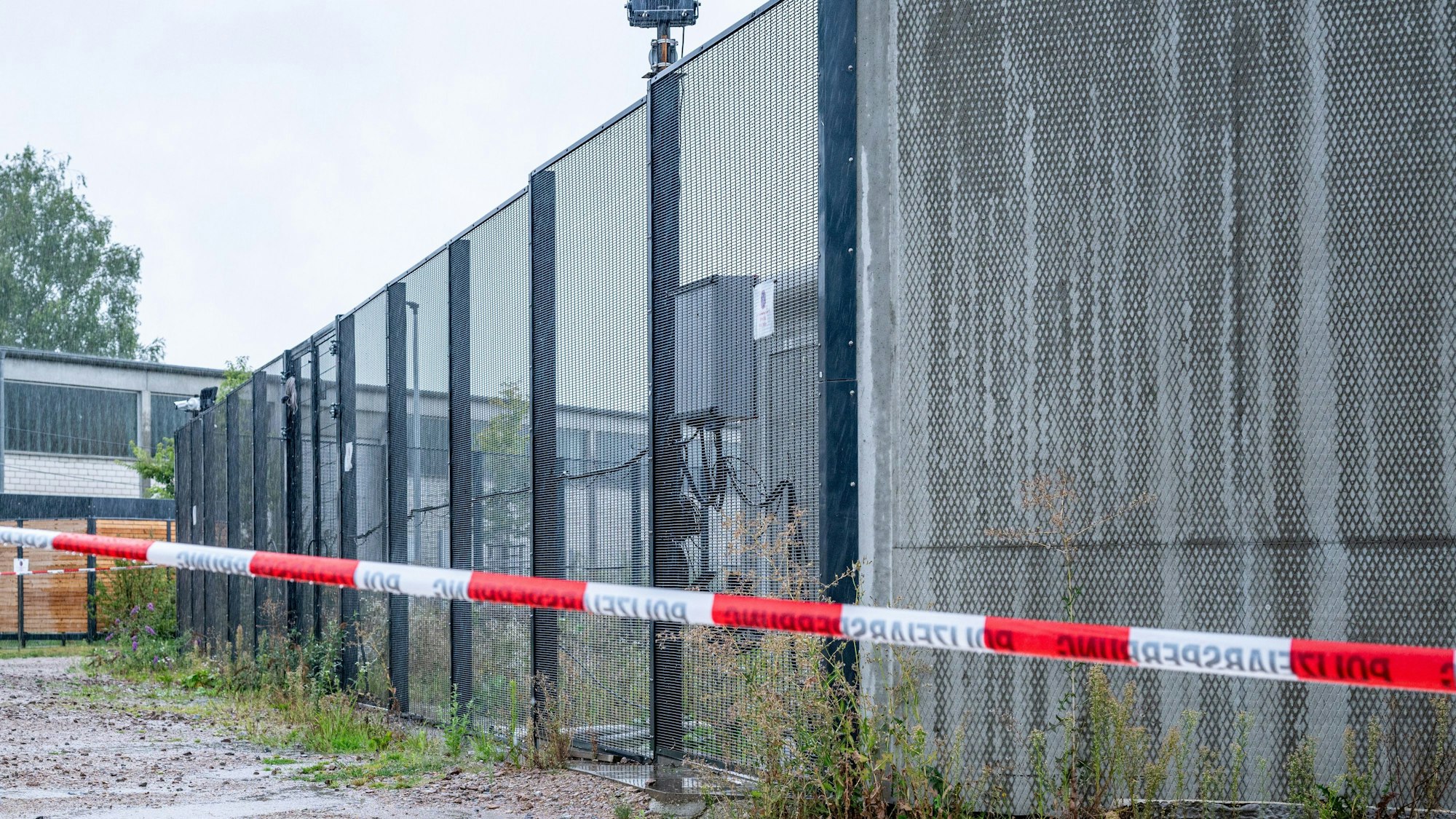 Ein Absperrband der Polizei ist vor einem Tor des Bezirkskrankenhauses Straubing angebracht. Vier Männer sind am Samstagabend im niederbayerischen Straubing aus der geschlossenen Klinik entflohen. Laut Polizei laufen umfangreiche Fahndungsmaßnahmen.