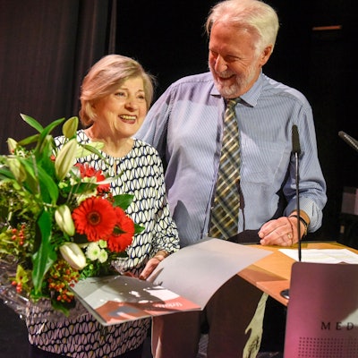 Eine Frau hält einen großen Blumenstraße in der Hand, neben ihr steht ein Man..