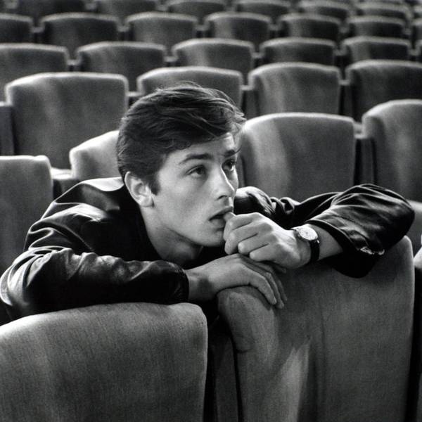Alain Delon sitzt auf einem Kinosessel und schaut auf die Leinwand.