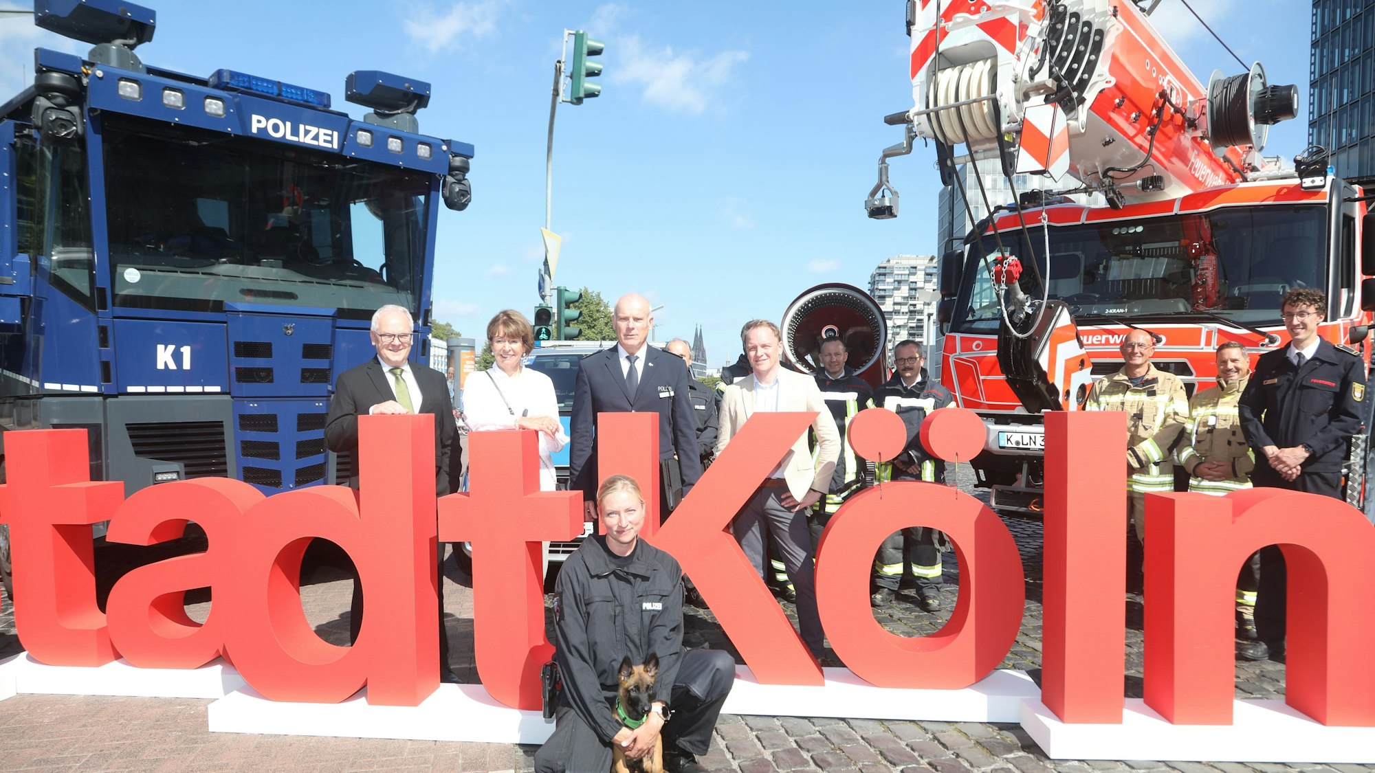 Henriette Reker, Oberbürgermeisterin von Köln, (2.v.l.) und Johannes Hermanns (l), Polizeipräsident stehen im Rheinauhafen mit Behördenvertretern vor dem Schriftzug der Stadt Köln zwischen Einsatzfahrzeugen.