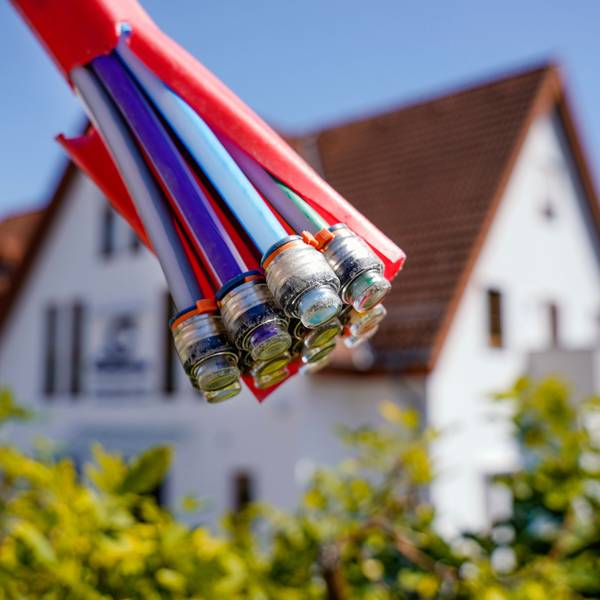 Ein Bündel mit Umhüllungen für Glasfaserkabel hängt vor einem Wohnhaus.