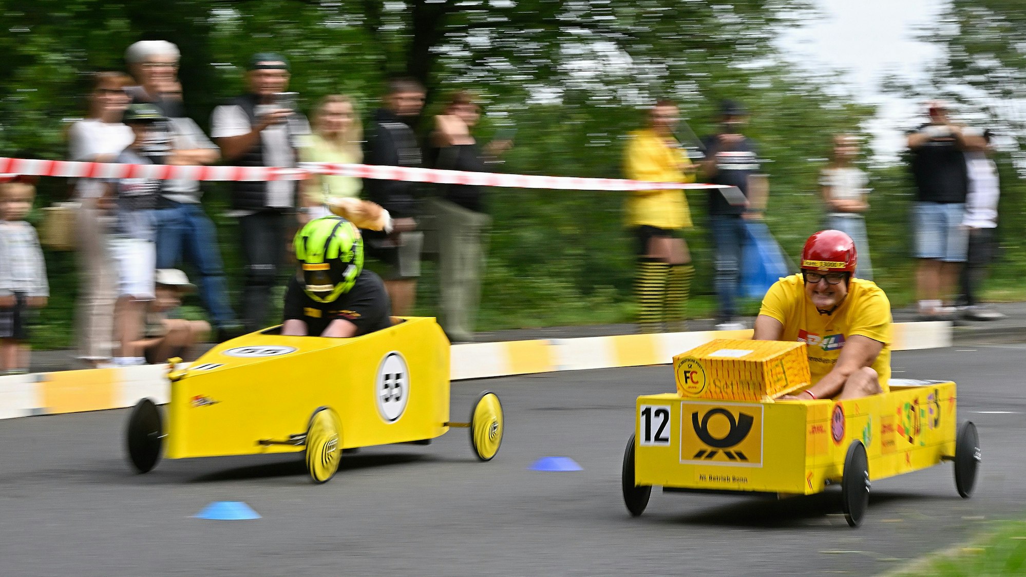 Jeweils zwei Piloten treten beim Seifenkistenrennen in Overath gut geschützt gegeneinen an.