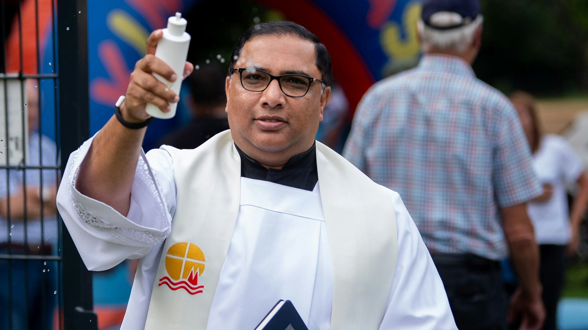 Das Bild zeigt den Pfarrer, der Weihwasser aus einer Plastikflasche verteilt.