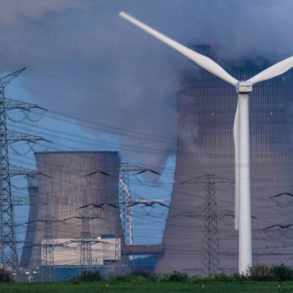 Dampf steigt aus dem RWE Braunkohlekraftwerk Neurath. Im Vordergrund steht eine Windkraftanlage. Auch NRW muss die CO2-Emissionen deutlich reduzieren.