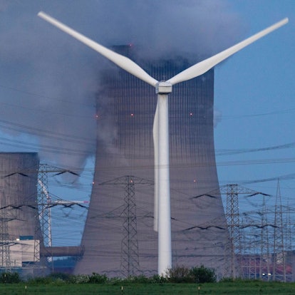 Dampf steigt aus dem RWE Braunkohlekraftwerk Neurath. Im Vordergrund steht eine Windkraftanlage. Auch NRW muss die CO2-Emissionen deutlich reduzieren.