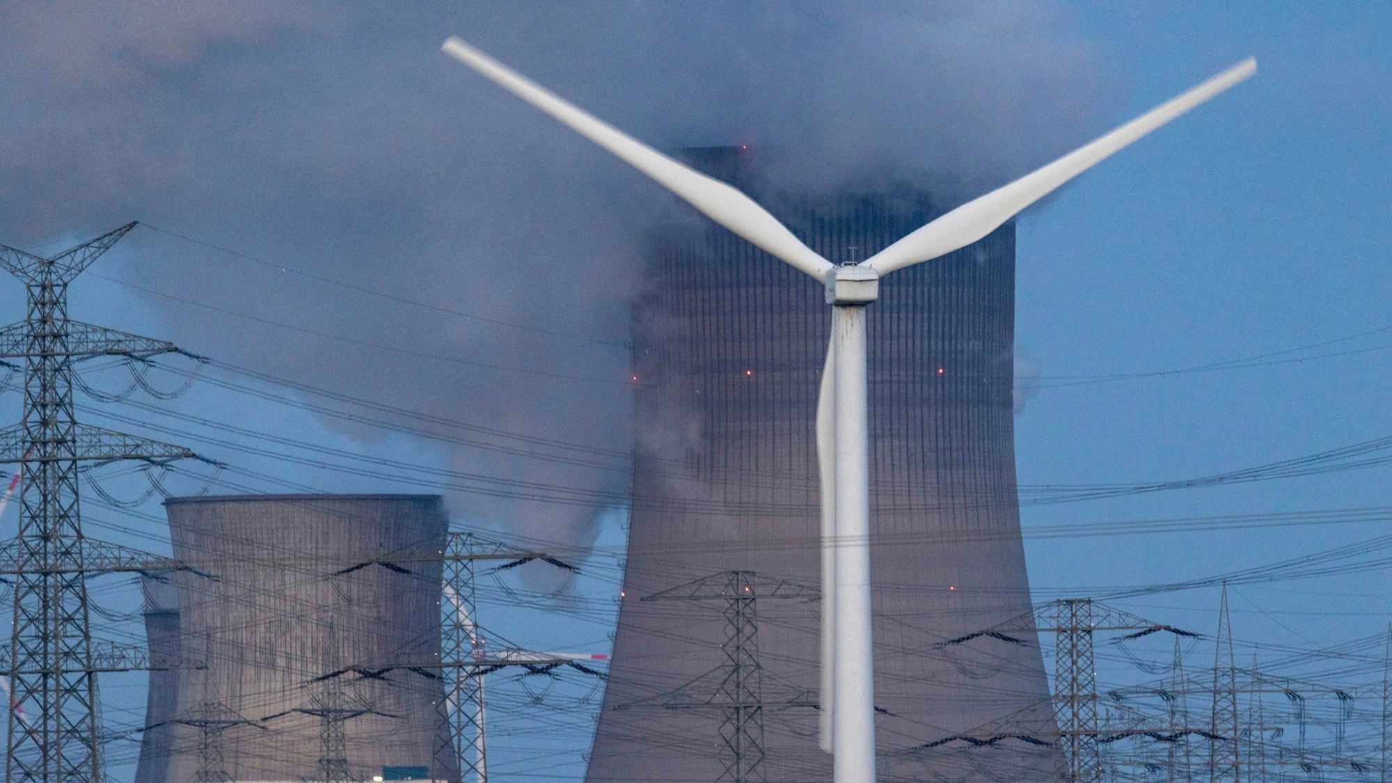 Dampf steigt aus dem RWE Braunkohlekraftwerk Neurath. Im Vordergrund steht eine Windkraftanlage. Auch NRW muss die CO2-Emissionen deutlich reduzieren.