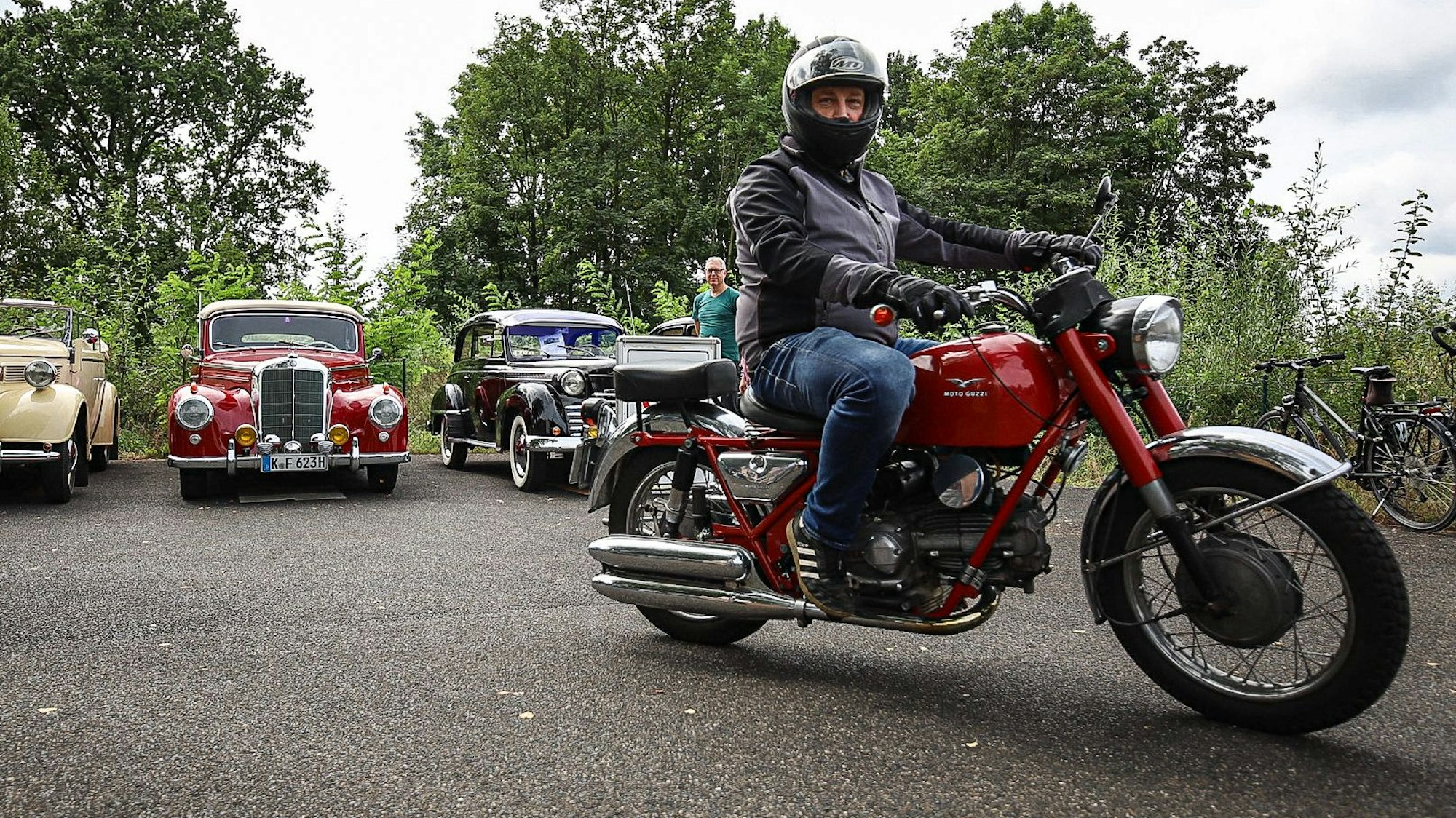 Ein Mann fährt auf einem historischen Motorrad an Oldtimern vorbei.