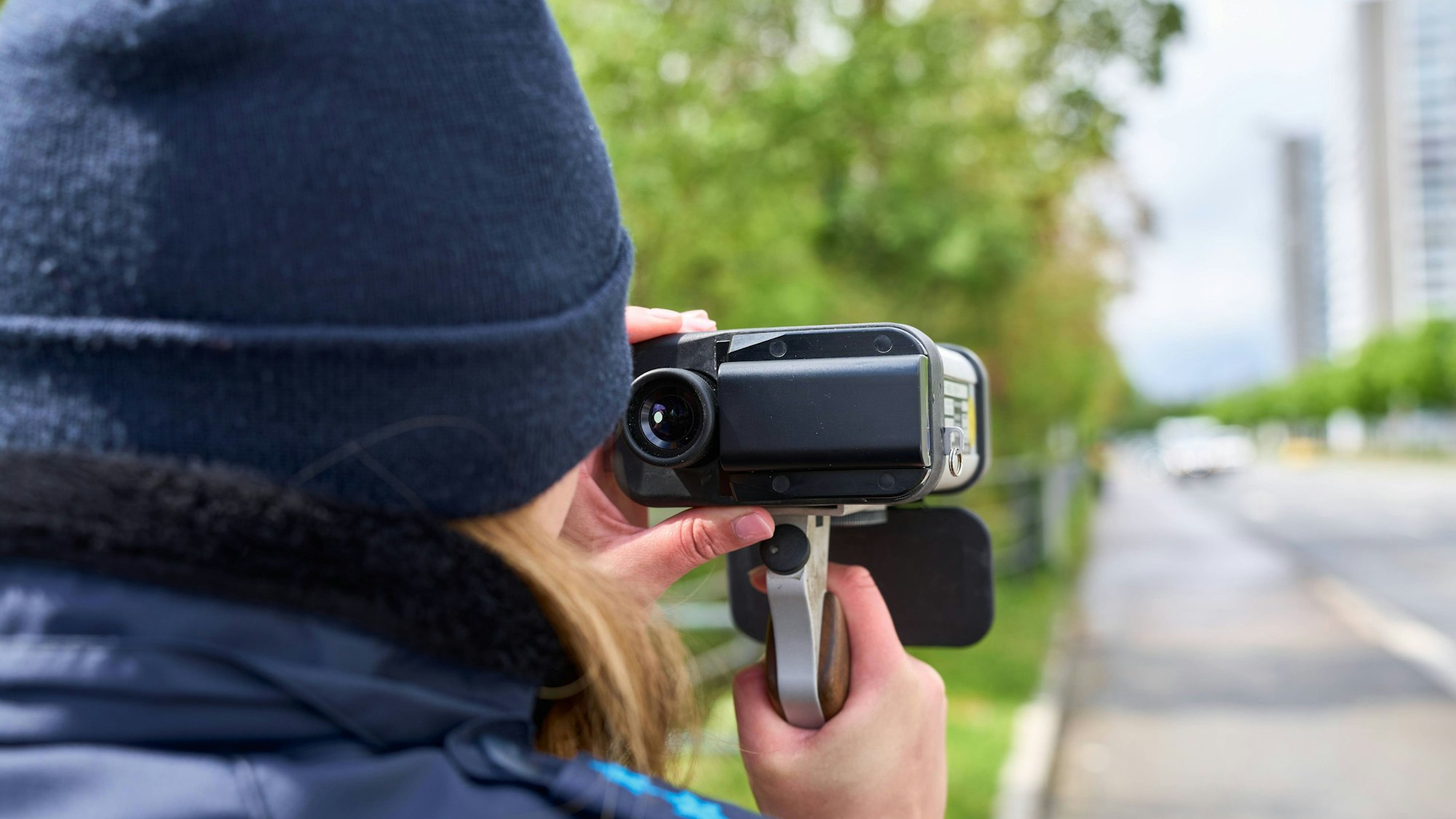 Eine Polizistin ist von hinten zu sehen, sie schaut durch ein Messgerät auf den Straßenverkehr.