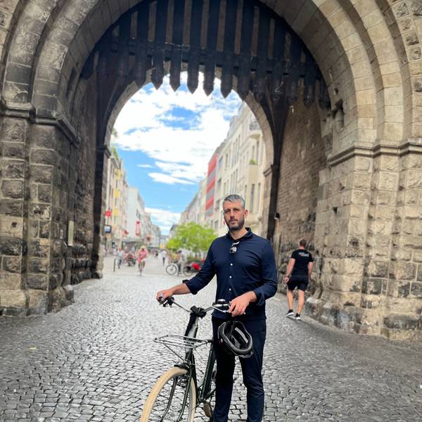 German Moyzhes steht mit einem Fahrrad vor der Severinstorburg.