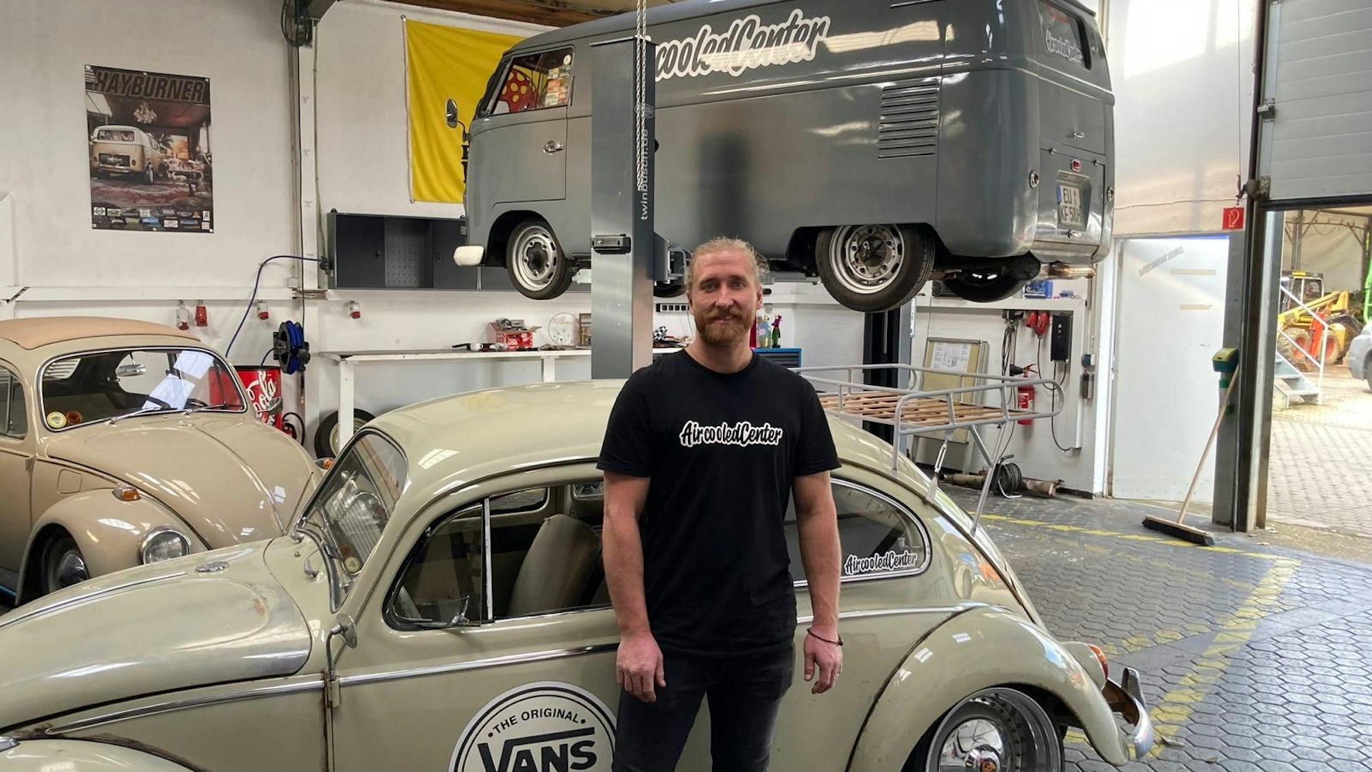 Ein Mann steht vor einem VW-Käfer in einer Werkstatt.