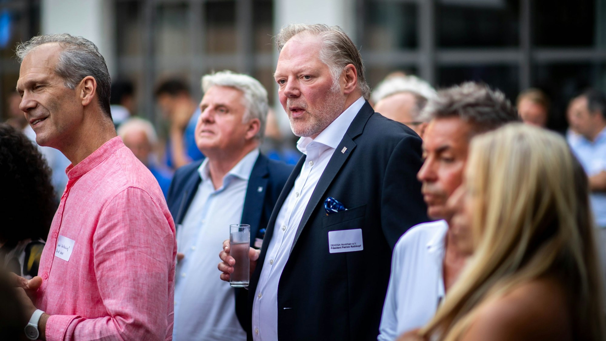 Das Bild zeigt Patrick Rothkopf, der ein Glas Wasser in der Hand hält. Um ihn herum stehen einige Gäste der Dehoga-Lounge.
