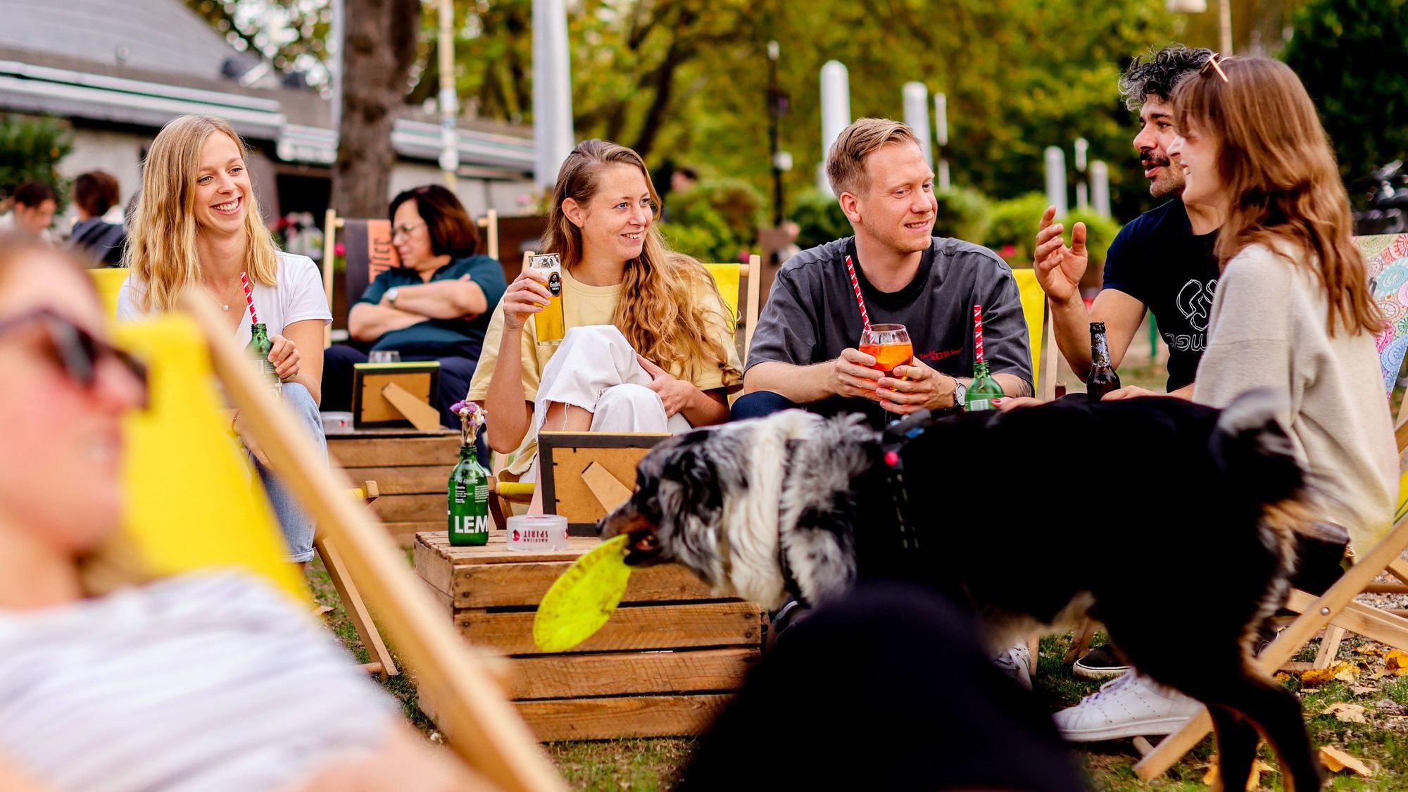 Young people sit in the beer garden at Aachener Weiher in Cologne in sunny and warm weather.