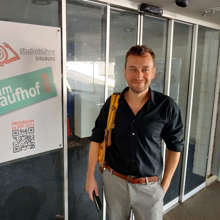 Ein Mann neben einem Plakat mit Aufschrift Studiobühne im Kaufhof