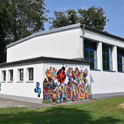 Turnhalle der Grundschule. Eine weiße Wand zeigt ein buntes Grafitto.