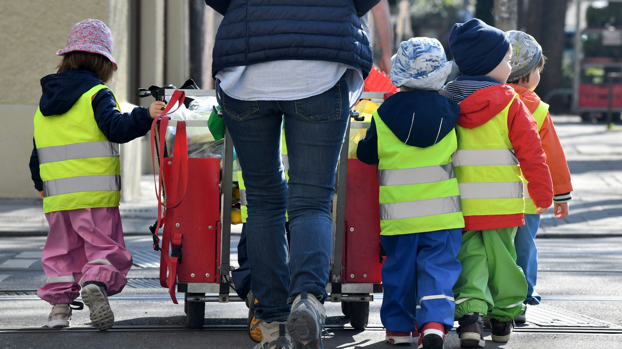 Ein Betreuerin läuft mit mehreren Kleinkindern über einen Bürgersteig.