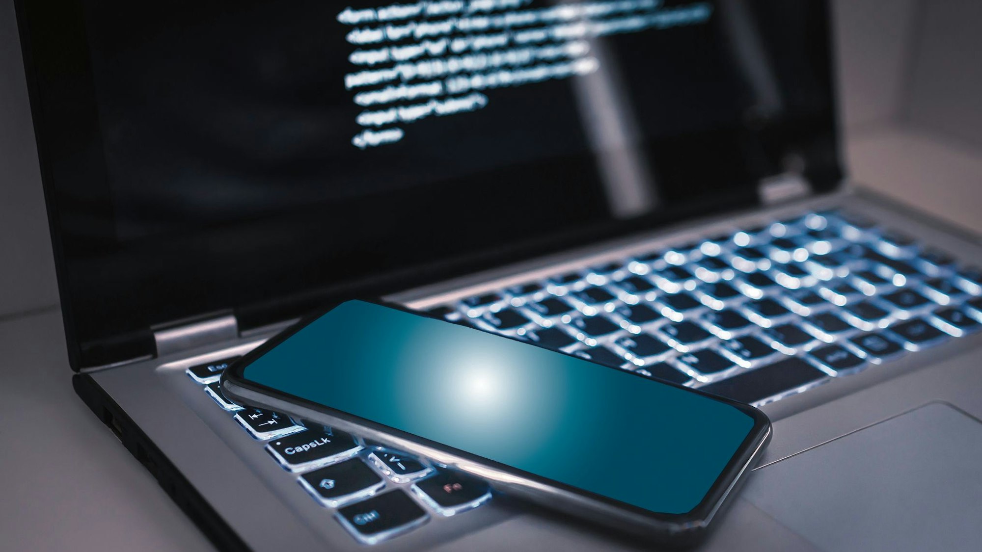 Ein Handy liegt auf der Tastatur eines Laptops.