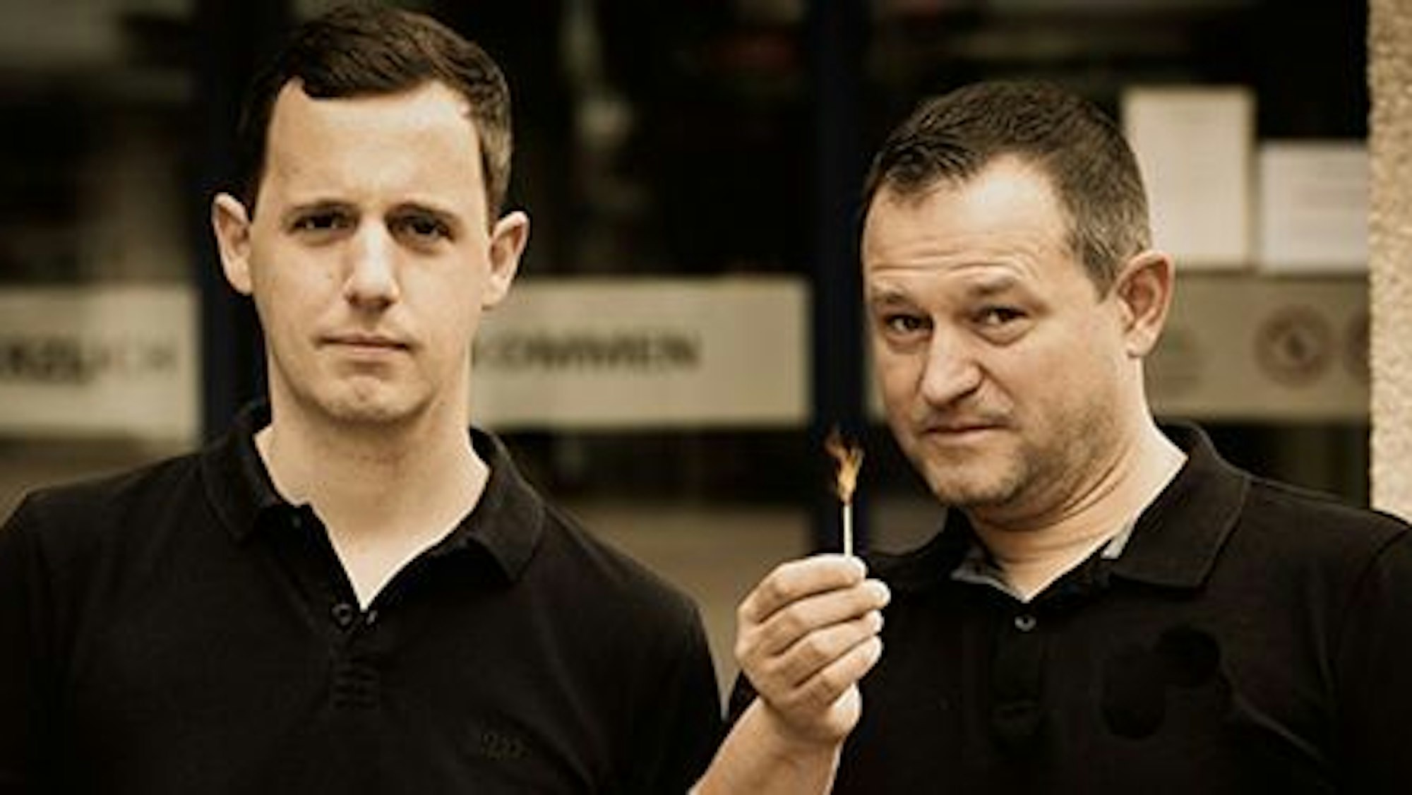 Jan Philipp Röser und Jürgen Bönsch stehen nebeneinander, Bönsch hält ein brennendes Streichholz in der Hand.
