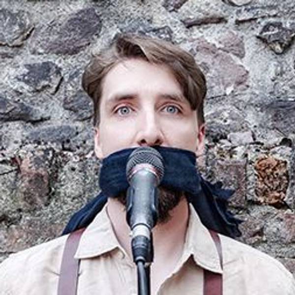 Juri von Stavenhagen hat ein Tuch über den Mund gebunden und steht hinter einen Mikrofon. .