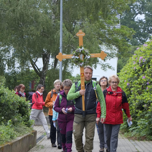 Pilgerinnen und Pilger ziehen hinter einem Mann her, der das Pilgerkreuz trägt.