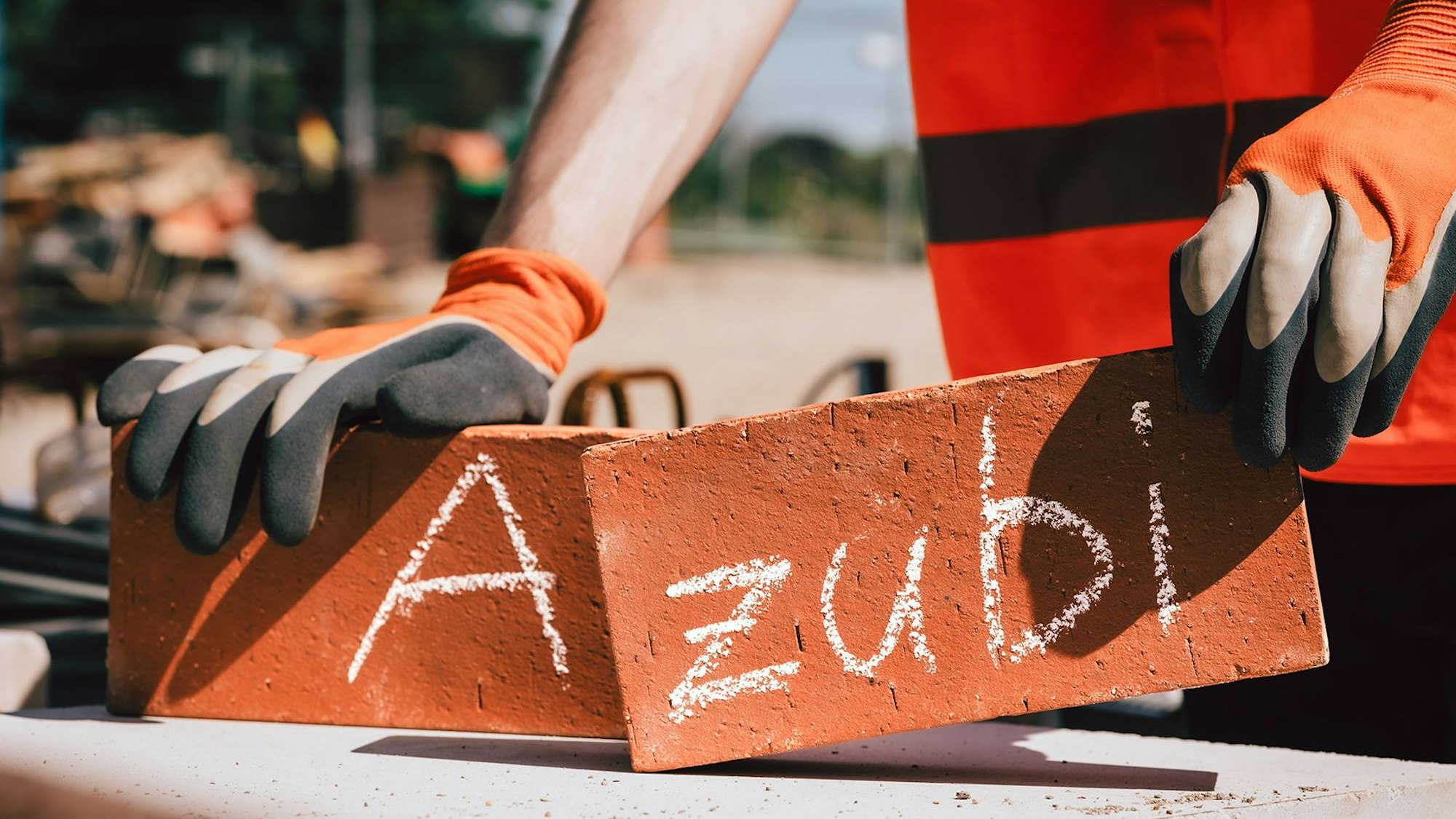 Ein Mann hält in jeder Hand einen Backstein, auf einem steht ein „A“, auf dem anderen der Schriftzug „zubi“.