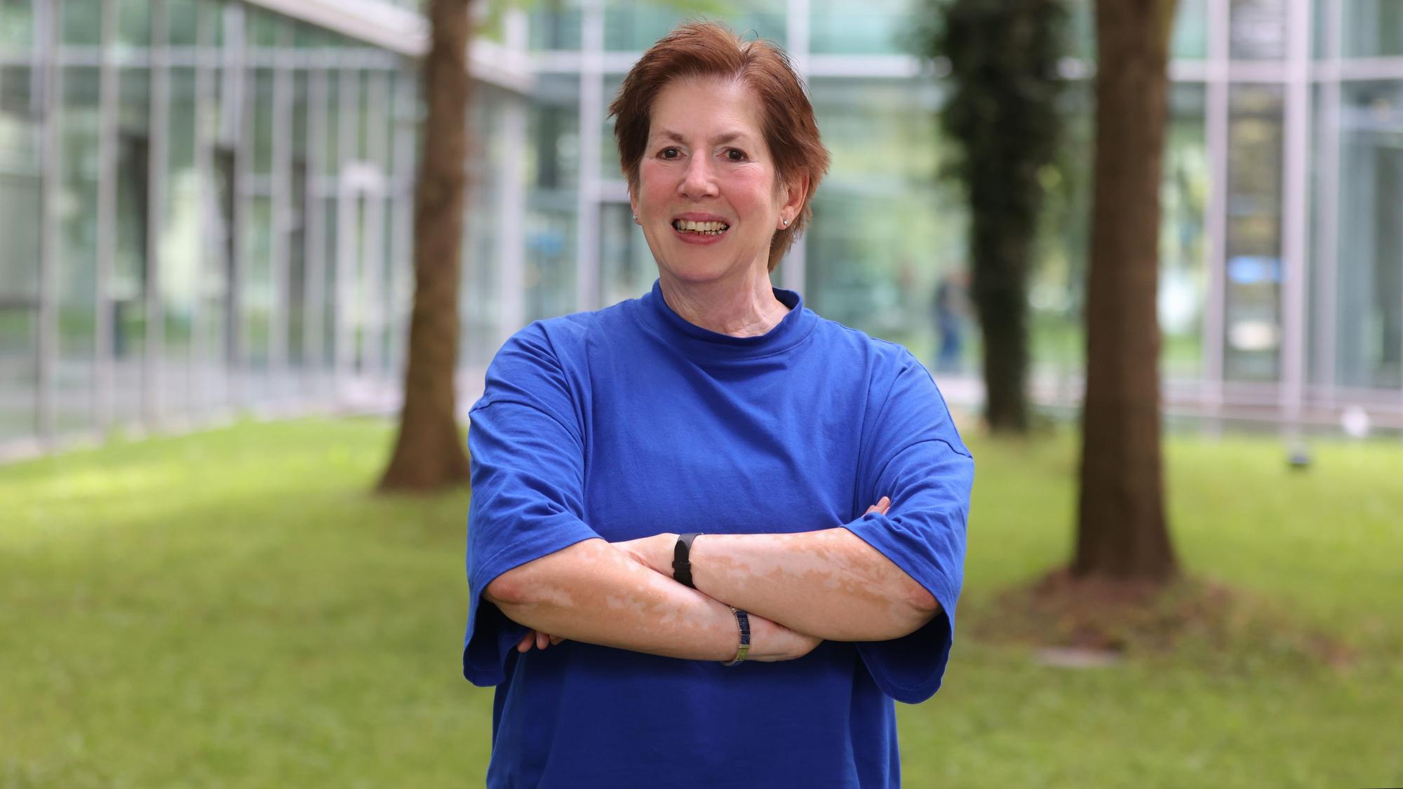 Petra Pluwatsch steht auf einer Wiese und lächelt in die Kamera. Sie trägt ein blaues T-Shirt.