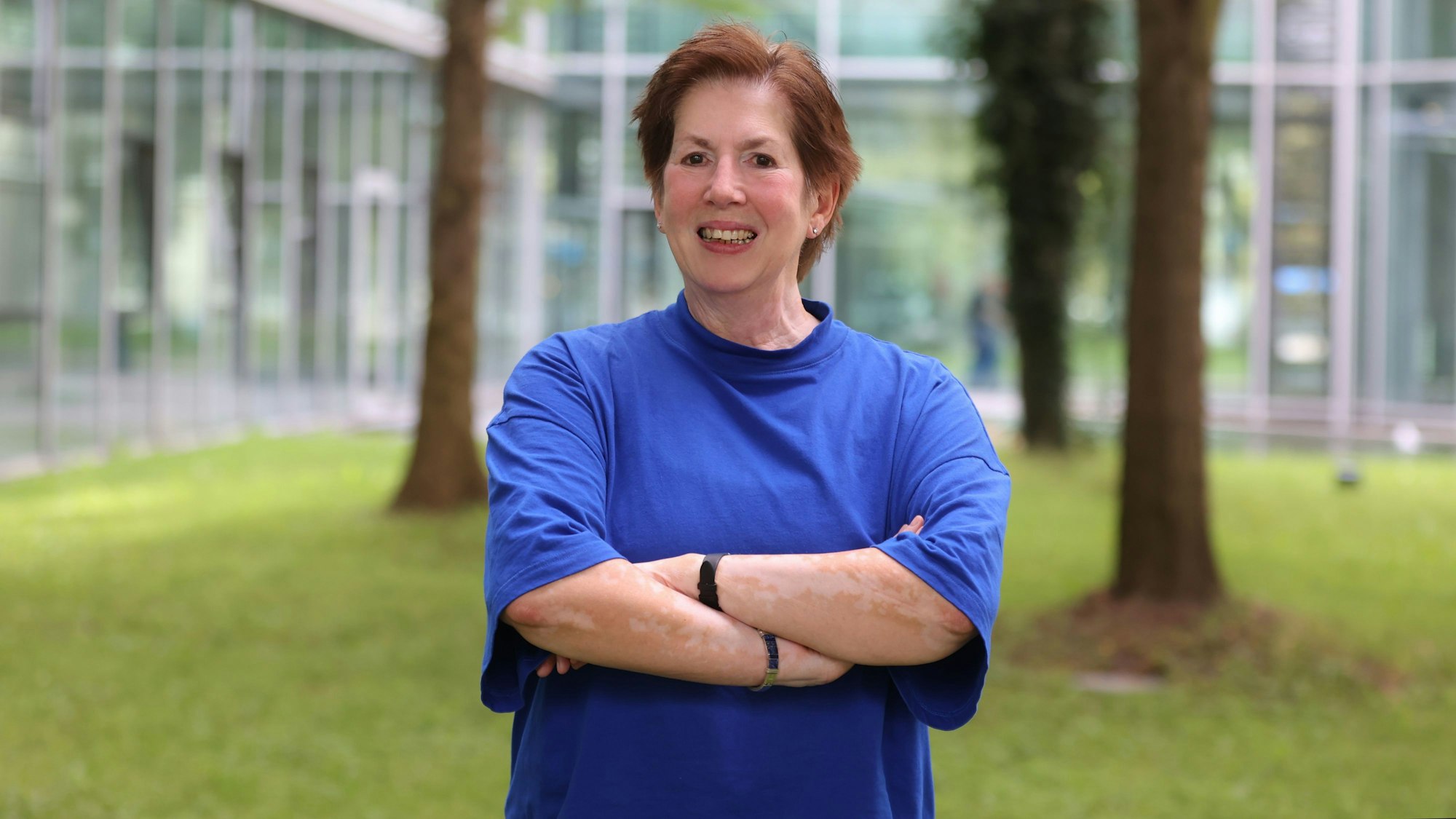 Petra Pluwatsch steht auf einer Wiese und lächelt in die Kamera. Sie trägt ein blaues T-Shirt.