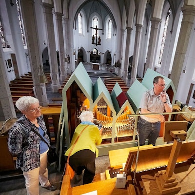 Organist Andreas Warler steht in der Mitte der Orgelempore in der Gemünder Kirche. Um ihn herum sind einige Besucher.