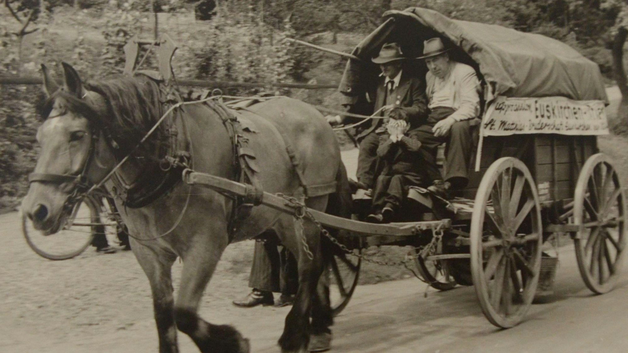 Ein Pferd zieht einen Planwagen, in dem zwei Männer sitzen.