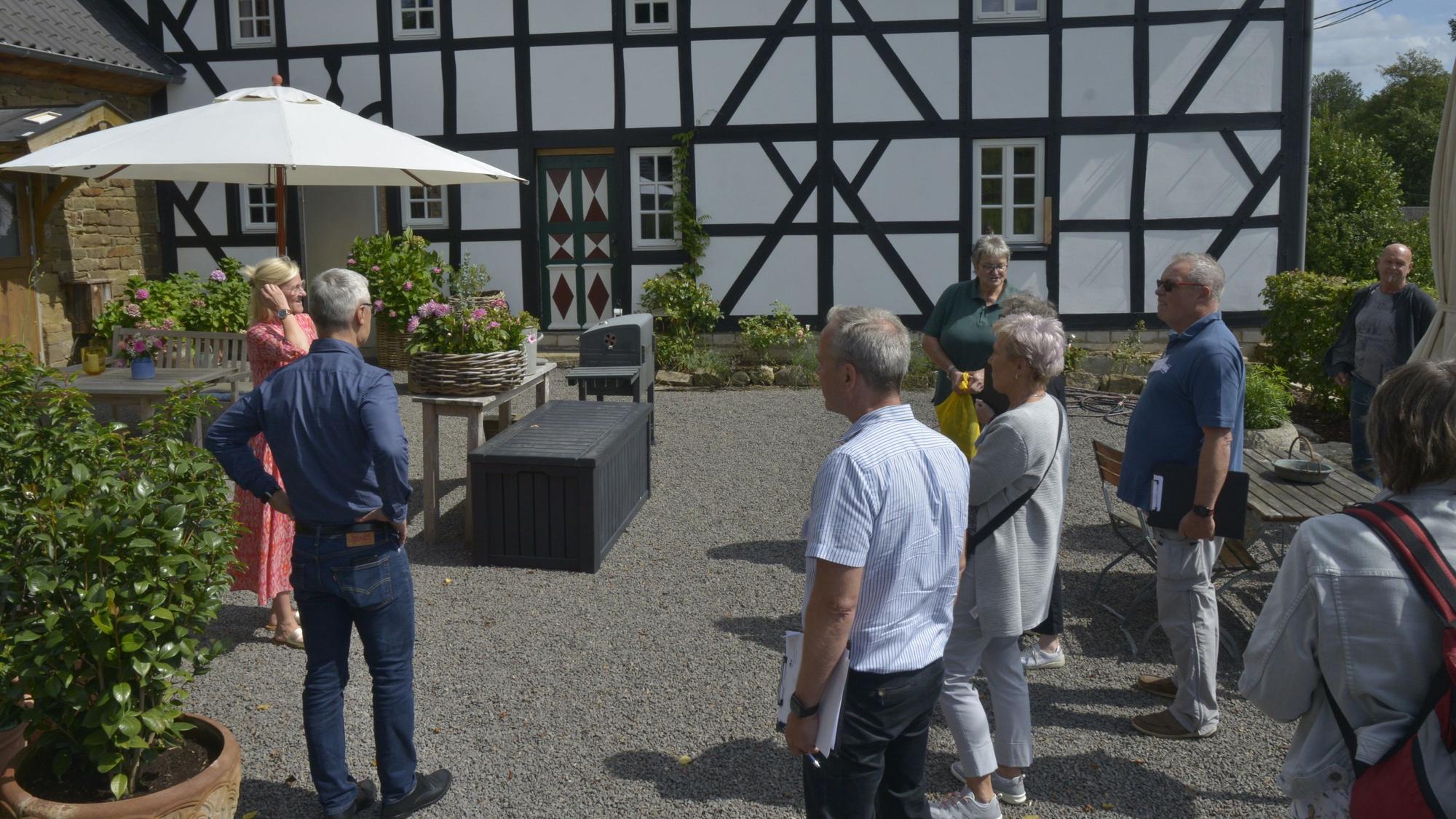 Dörfliche Idylle mit blühenden Gärten und alten Fachwerkhäusern. Eine Gruppe schaut sich den Ort an.