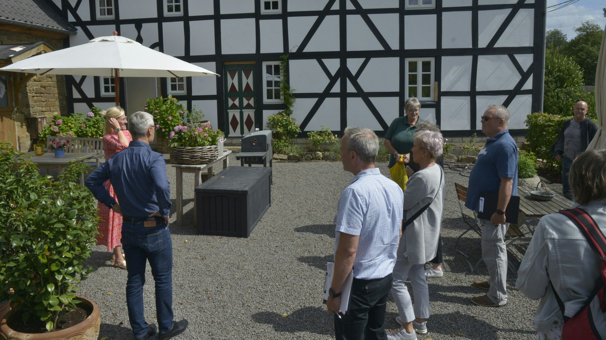 Dörfliche Idylle mit blühenden Gärten und alten Fachwerkhäusern. Eine Gruppe schaut sich den Ort an.