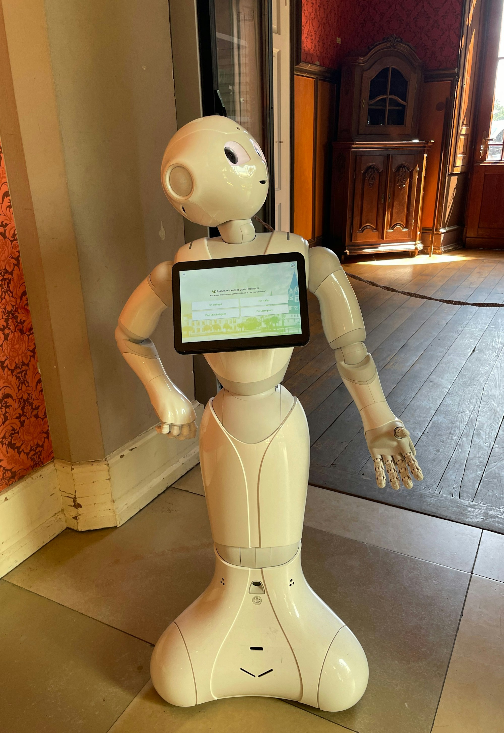 Ein kleiner Roboter mit Bildschirm auf der Brust steht in einem Museumsraum.