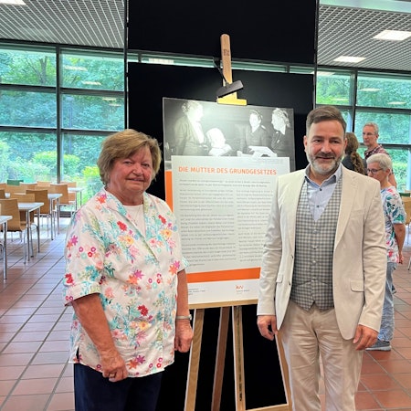 Die beiden stehen nebeneinander vor einer der Informationstafeln.