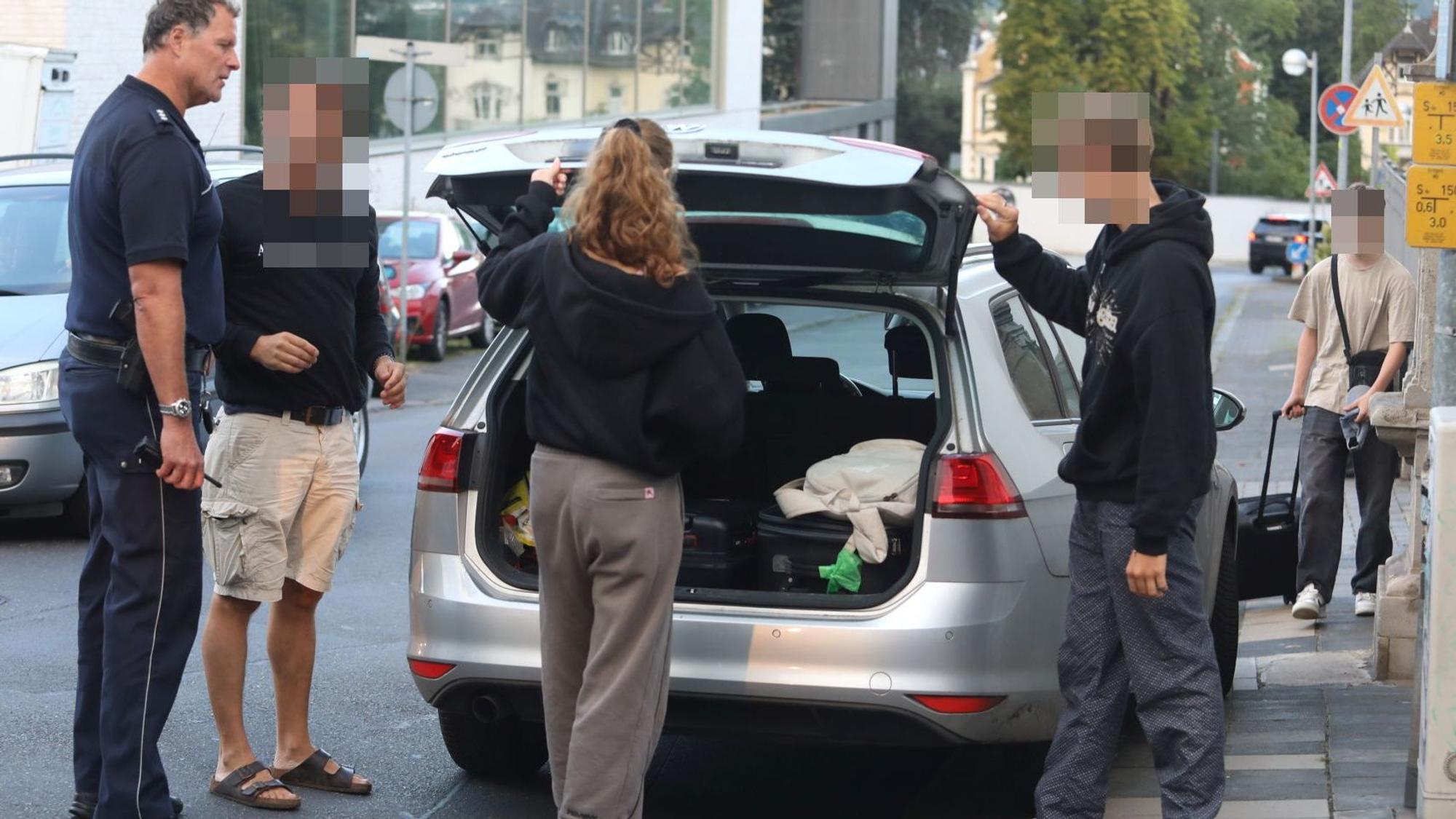 Vier Personen, darunter ein Polizeibeamter, stehen an einem Auto, dessen Heckklappe geöffnet ist.