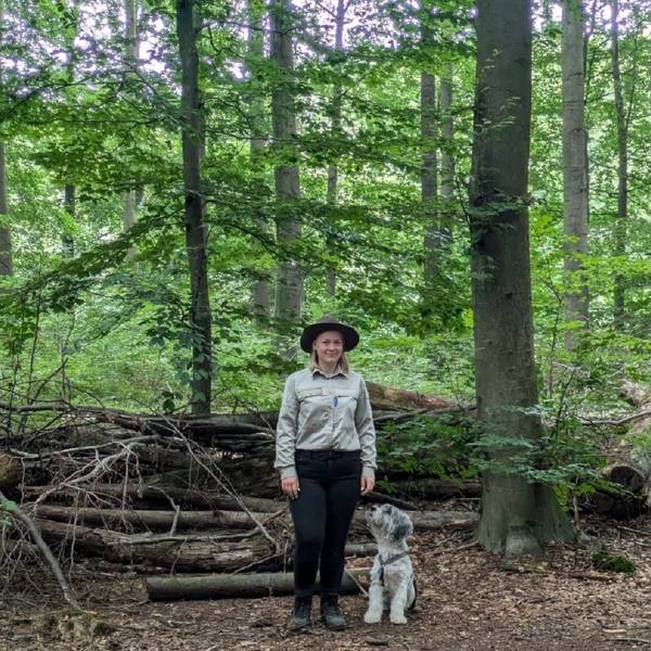 Auf dem Bild ist eine Waldhüterin mit ihrem Hund zu sehen.