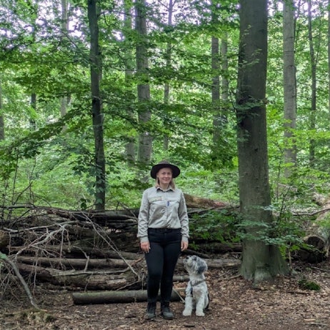 Auf dem Bild ist eine Waldhüterin mit ihrem Hund zu sehen.