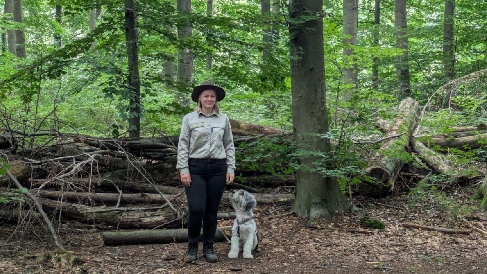 Auf dem Bild ist eine Waldhüterin mit ihrem Hund zu sehen.